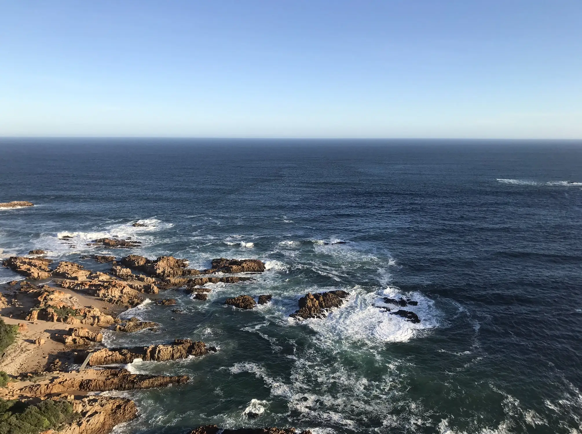 The Garden Route coastline from above: sandstone rocks and breaking surf below a clear sky and open sea
