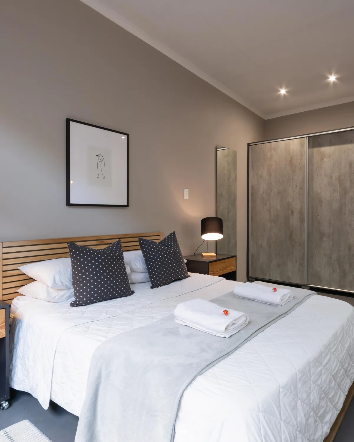 A bedroom made up for an arrival, fresh towels folded on the bed and a bedside lamp on