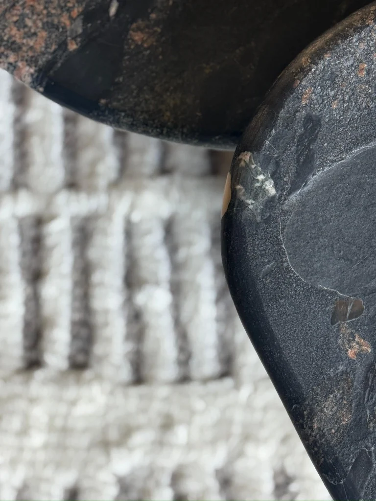 A dark stone piece with a honed edge resting on a textured woven textile
